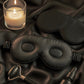 Black sleep mask, candle, and bottle on black satin fabric