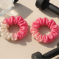 Two pink hair scrunchies with a water bottle and dumbbells on a beige surface